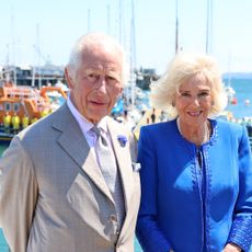 King Charles and Queen Camilla standing in front of some boats 