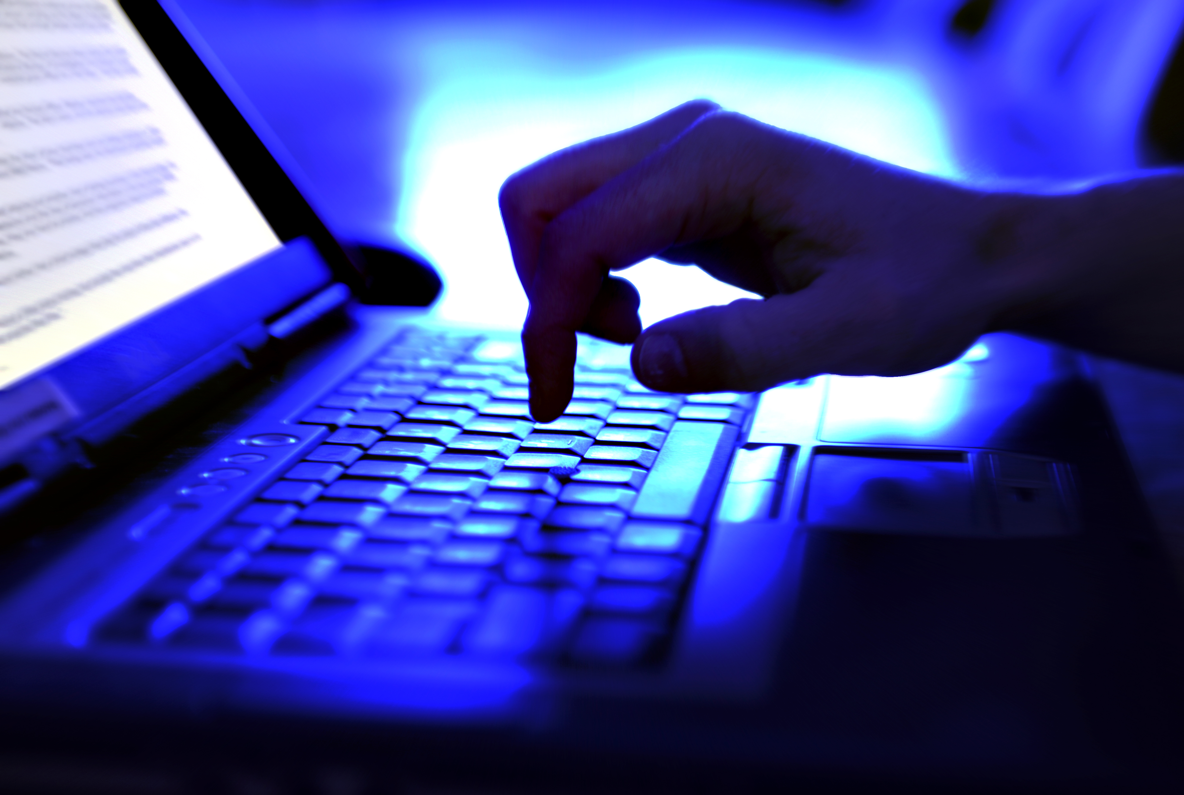 person typing on keyboard in blue-lit room