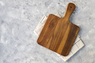 A wooden chopping board on top of a patterned tea towel and marble surface.