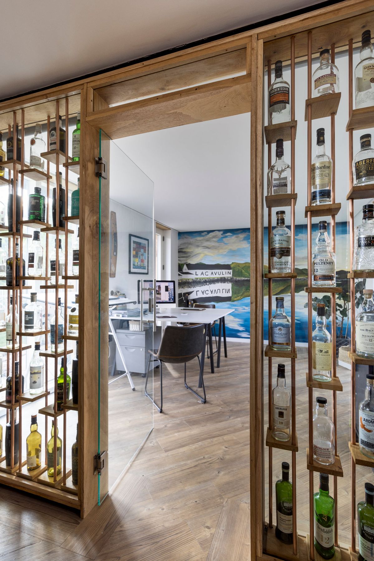A home office with glass walls containing empty whiskey bottles