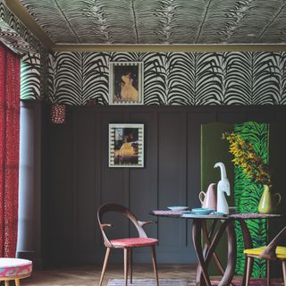 A dining room with dark panelled walls and an animal-print wallpapered ceiling