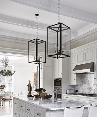 All white kitchen with kitchen island along the centre and metal frame rectangular lantern ceiling lights