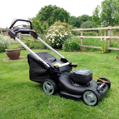 The WORX WG749E 46cm Cordless Self-Propelled Lawn Mower on a green lawn with a fence behind