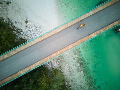 A drone shot of a cyclist riding across a bridge over a Slovenian river