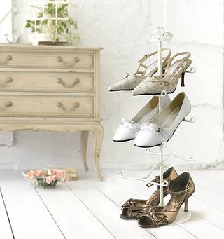 Tiara Heels Shoe Rack four tier white metal rack with pairs of womens shoes on it, in a white room with an elegent chest of drawers behind it