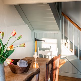 A staircase painted in Farrow & Ball's Pigeon shade with an antigue dining table and mismatched chairs next to it