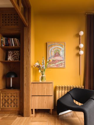 A corner in a living room with wooden floors and furniture, and a yellow painted wall