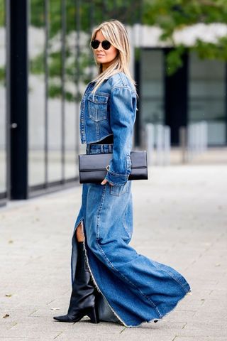 A street style shot of a woman wearing a denim outfit with boots