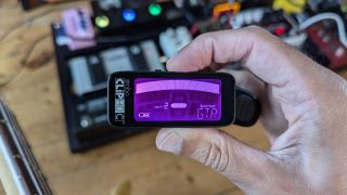 A man holds a Peterson Stroboclip HDC clip on guitar tuner over a pedalboard