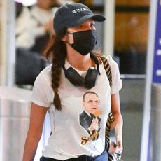 Olivia Rodrigo spotted arriving at JFK airport in New York City wearing a Frank Sinatra 1979 Tour shirt, a Winona hat, blue barrel jeans, and Adidas sneakers. 