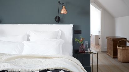Grey bedding on double bed with bedside table and white vase in front of grey wall