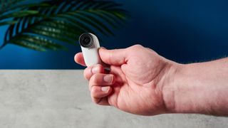 A photo of the Insta360 Go 3S thumb camera being held between a person's fingers.