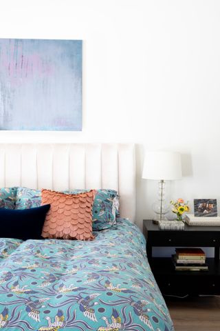 A white bedroom with colorful blue, bird-patterned bedding, a fabric scales throw pillow, and bedside table and