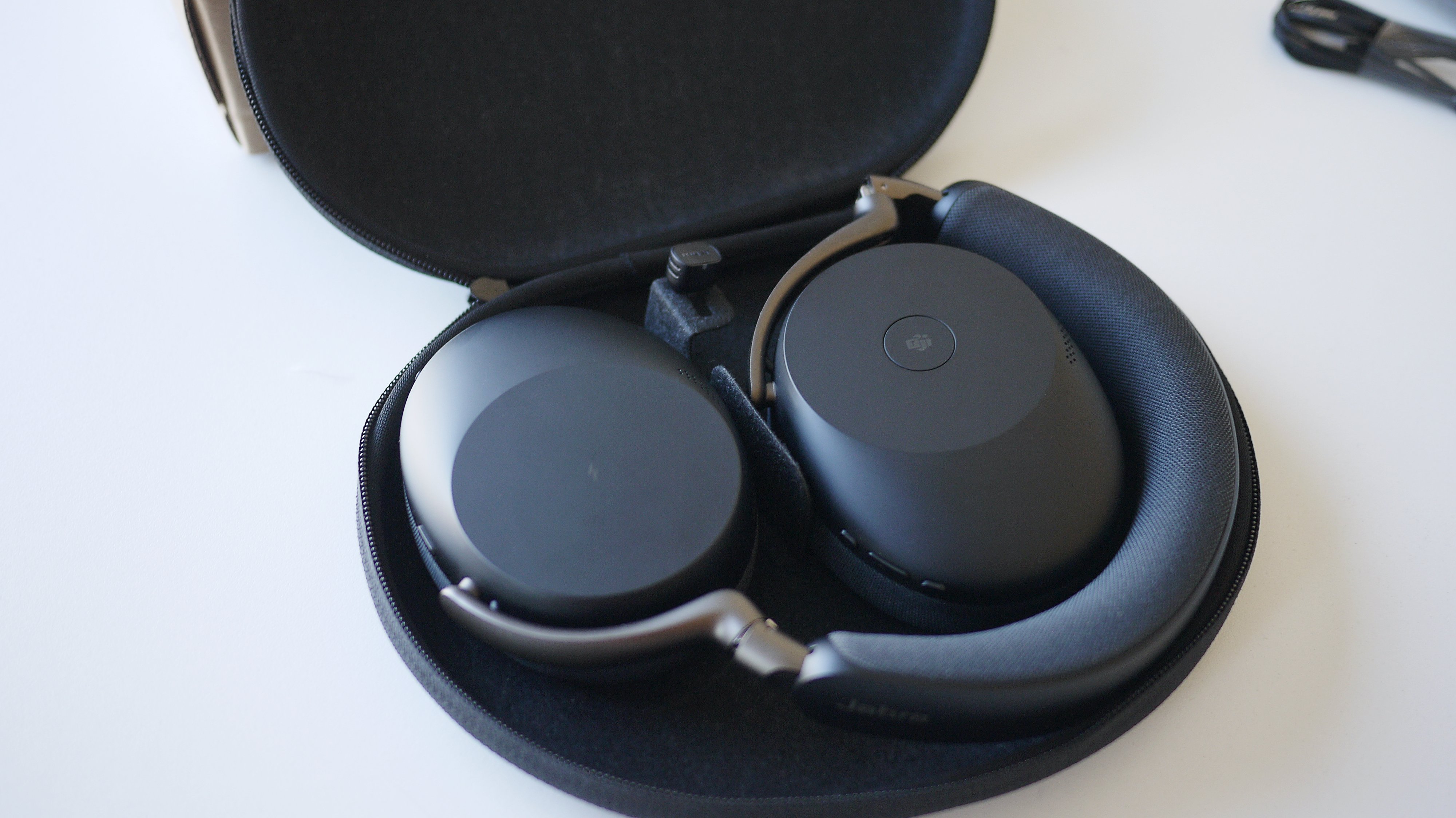 Jabra Evolve3 85 ligger i det &amp;aring;bne etui p&amp;aring; et bord.