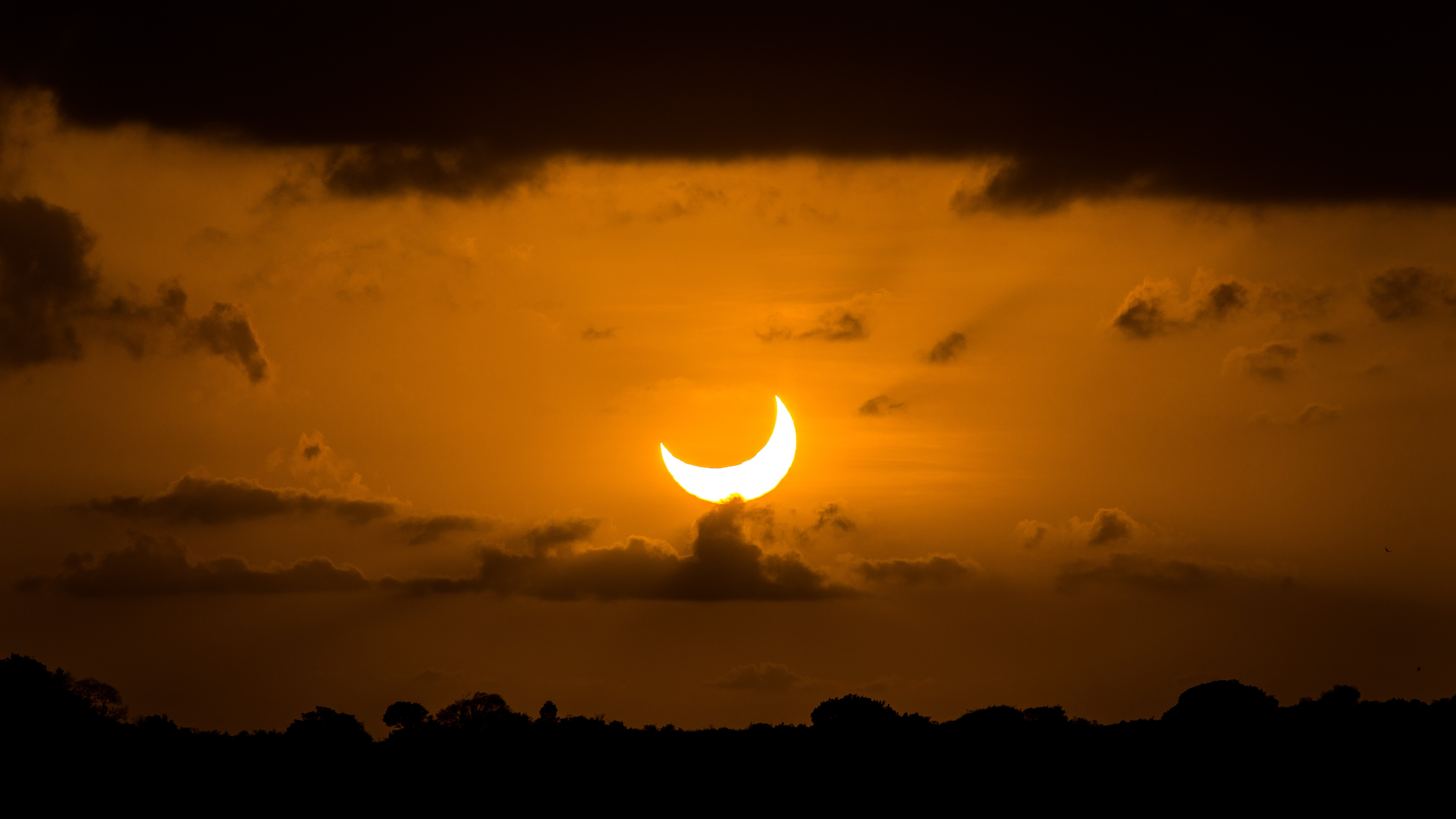 sun appears as a bright crescent in a sky that glows an orangey hue.