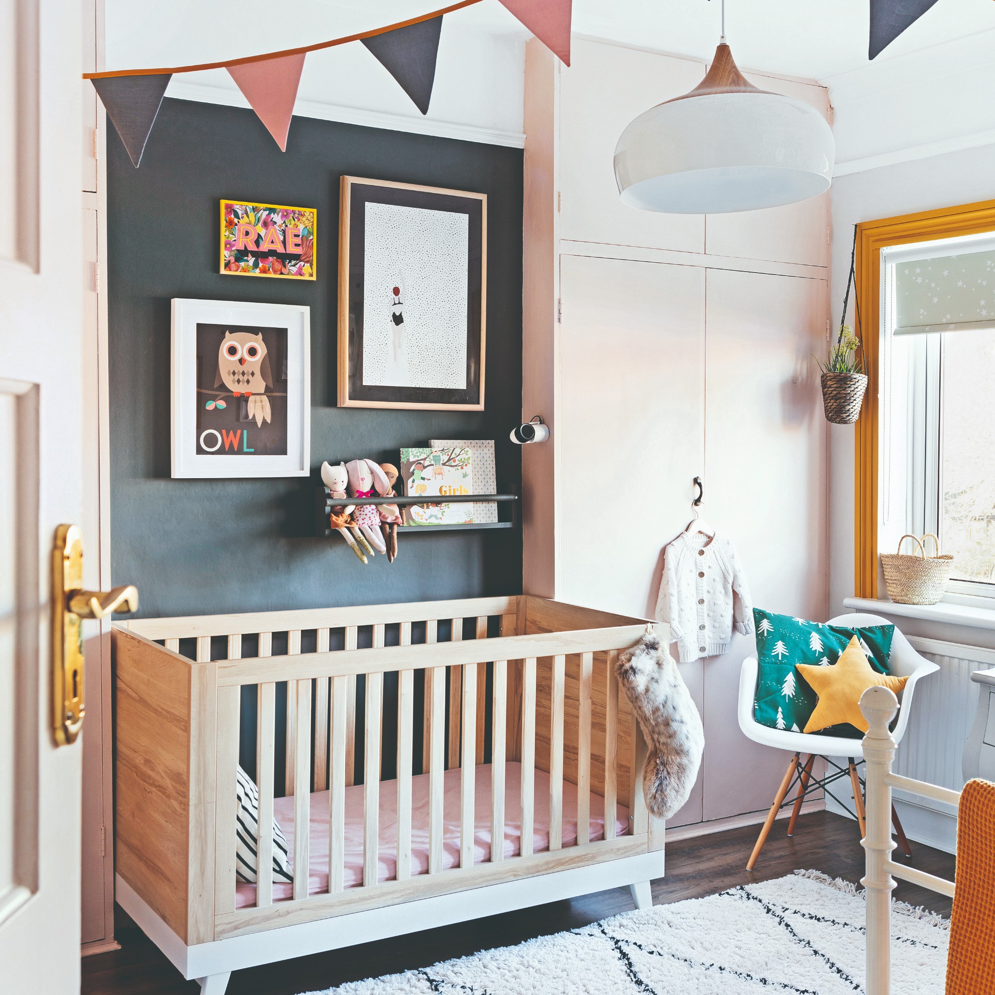 A nursery with patterned blinds and pink wardrobes built into alcoves