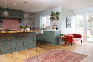 open plan kitchen and living area with pink wallpaper, green cabinets and velvet sofa