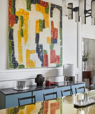 Colorful artwork on wall above blue console with select collection of vases and gilded top dining table