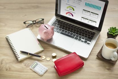 Piggy bank, laptop, purse with money, coffee cup on wooden table top