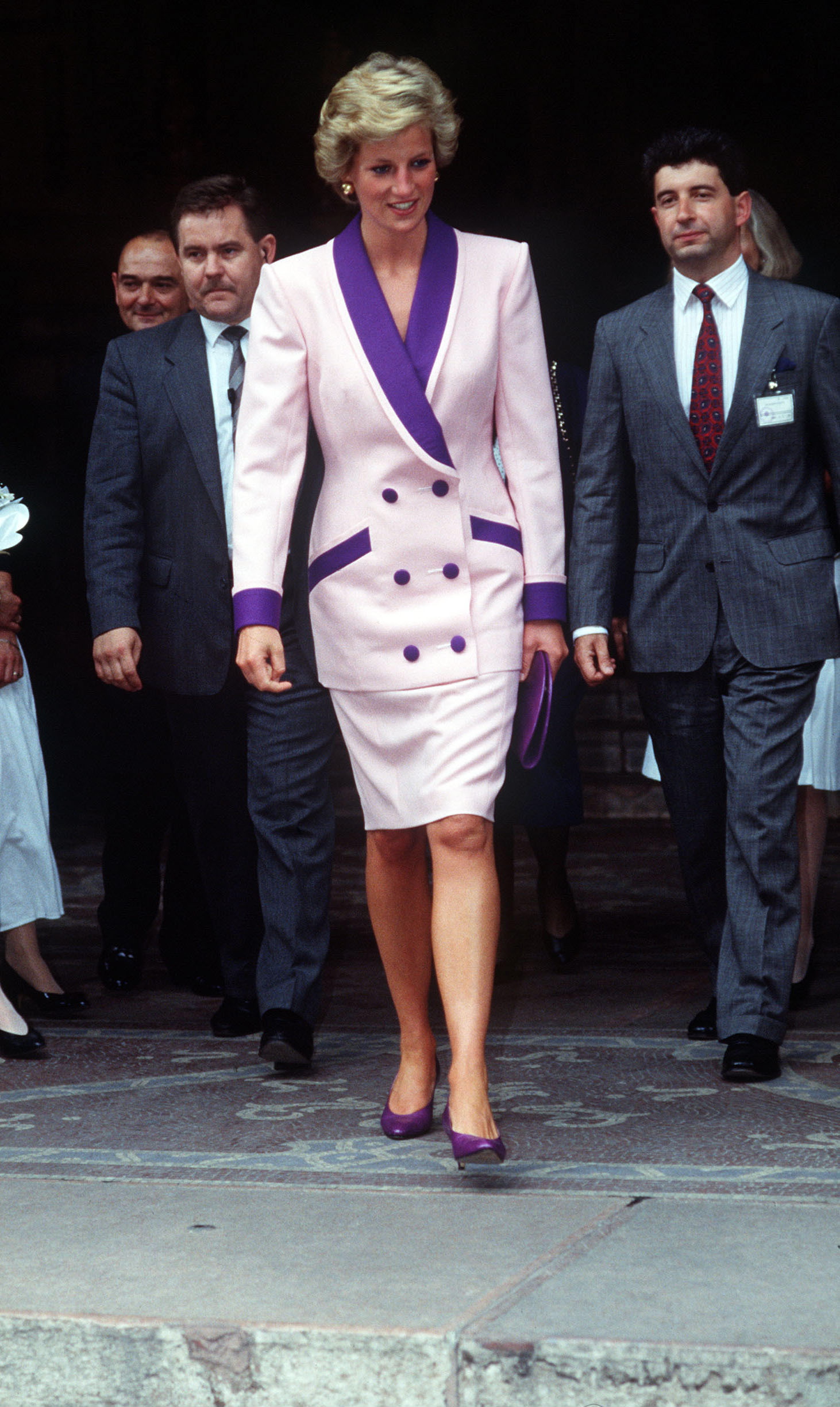 Princess Diana in Budapest, Hungary wearing a pink coat dress with purple accents, and her Private Secretary Patrick Jephson walking behind her