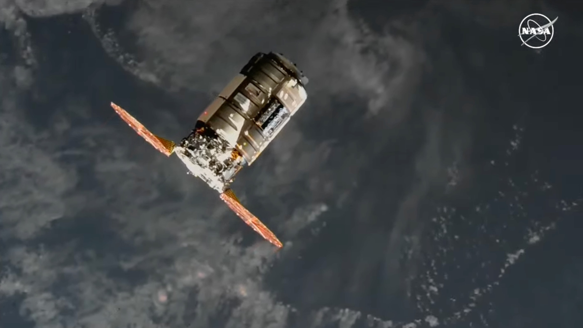 a cylindrical silver spacecraft is seen from above, with earth in the background