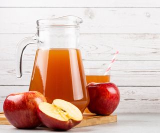 A pitcher of apple juice against a white background.