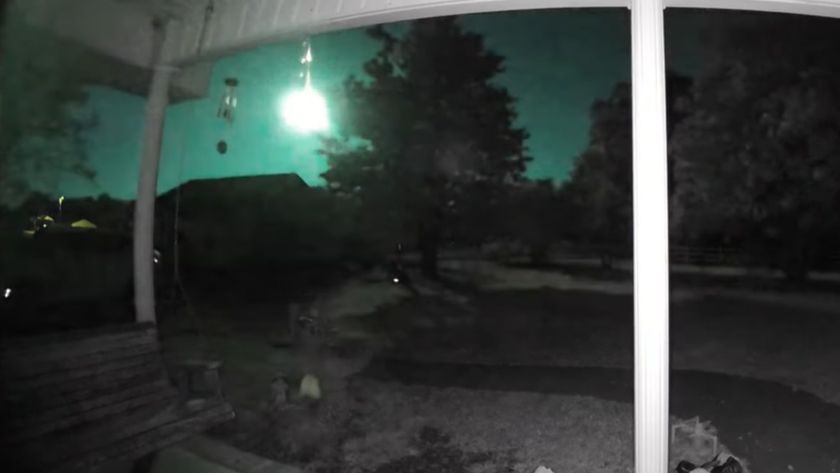 A green fireball meteorite is pictured exploding in the sky as seen from a wooden porch looking out into a garden.