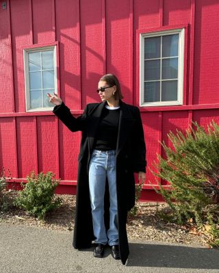 Hailey Bieber wearing a black Saint Laurent coat, black sweater, Levi's jeans, and square-toe loafers.