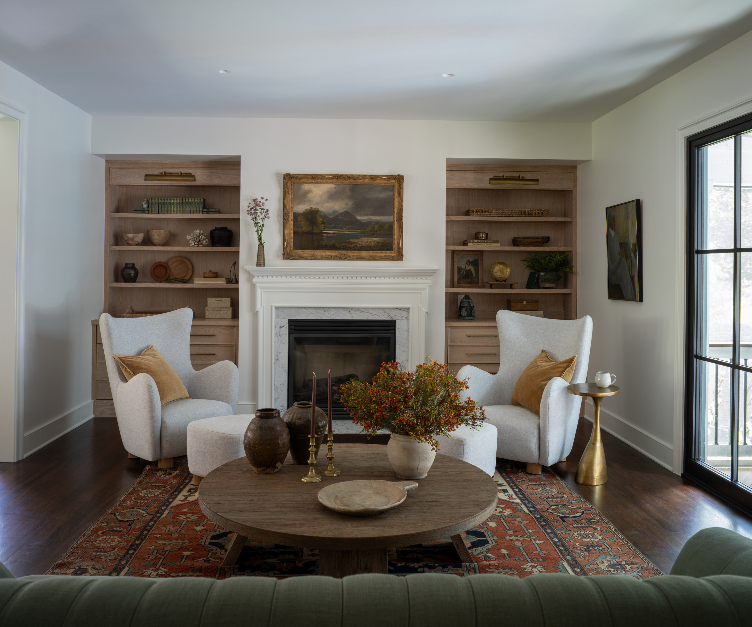 a formal sitting area with symmetrical bookshelves, decor on the shelves, a fireplace, winged back chairs, a coffee table with decor, and a large painting hanging above the fireplace