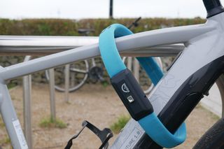 A blue squire straplok, locking an e-bike to a bike rack in a quiet park