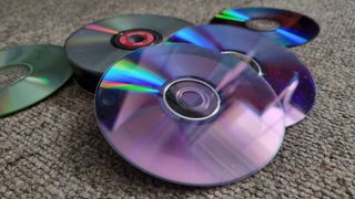 A collection of upturned CDs, DVDs and Blu-Rays on a carpeted floor