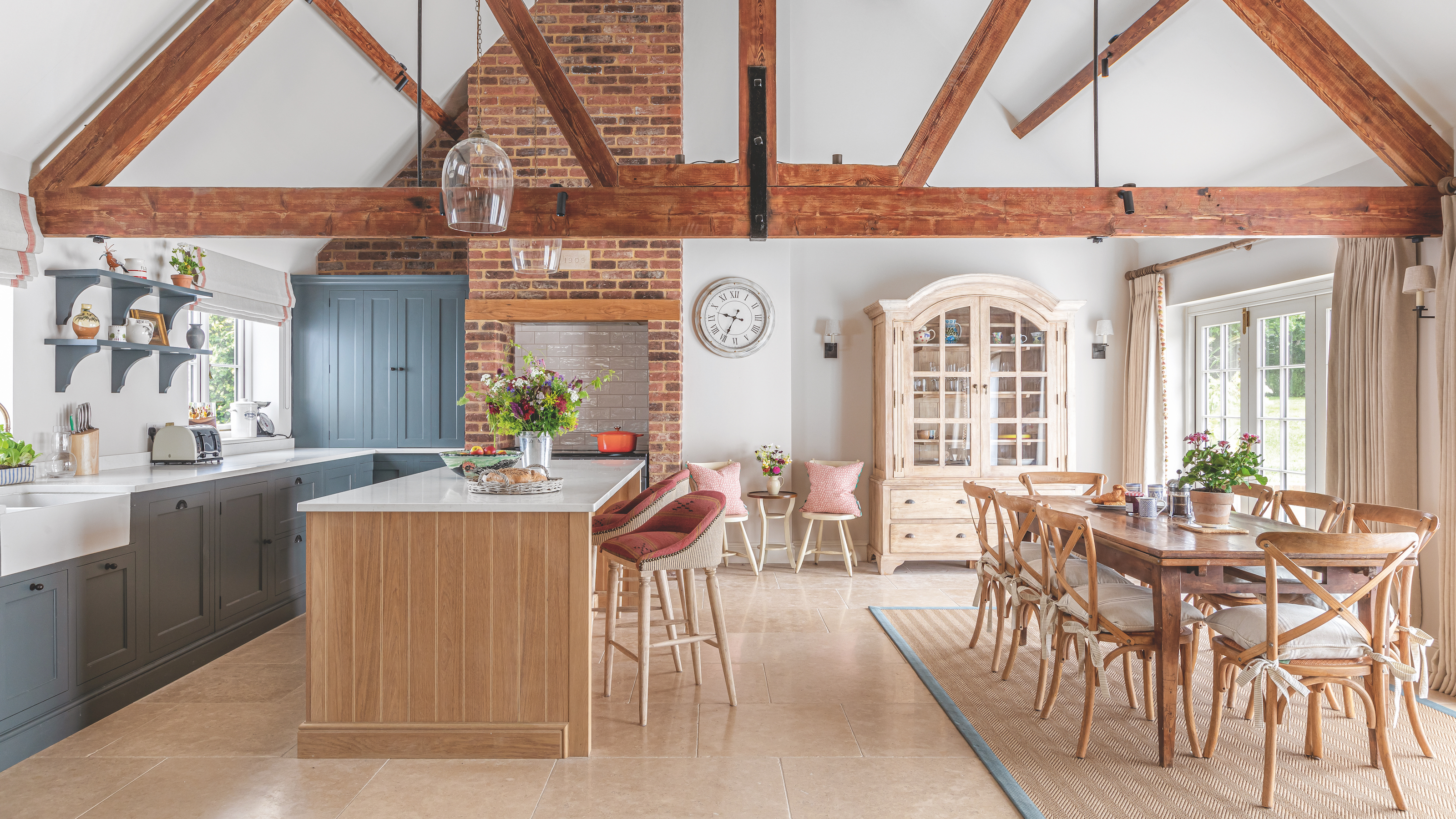 kitchen and dining area in barn conversion with wooden beams on ceiling and wooden island unit and blue cabinetry next to wooden farmhouse dining table with chairs