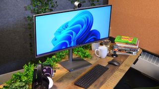 En HP Envy 34 står på ett träfärgat skrivbord med kontorsmaterial, en kaffekopp och en grön växt runtom.