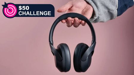 Tribit QuietPlus 81 held in a man's hand on pink background, with TechRadar's '$50 challenge' badge in the top-left corner