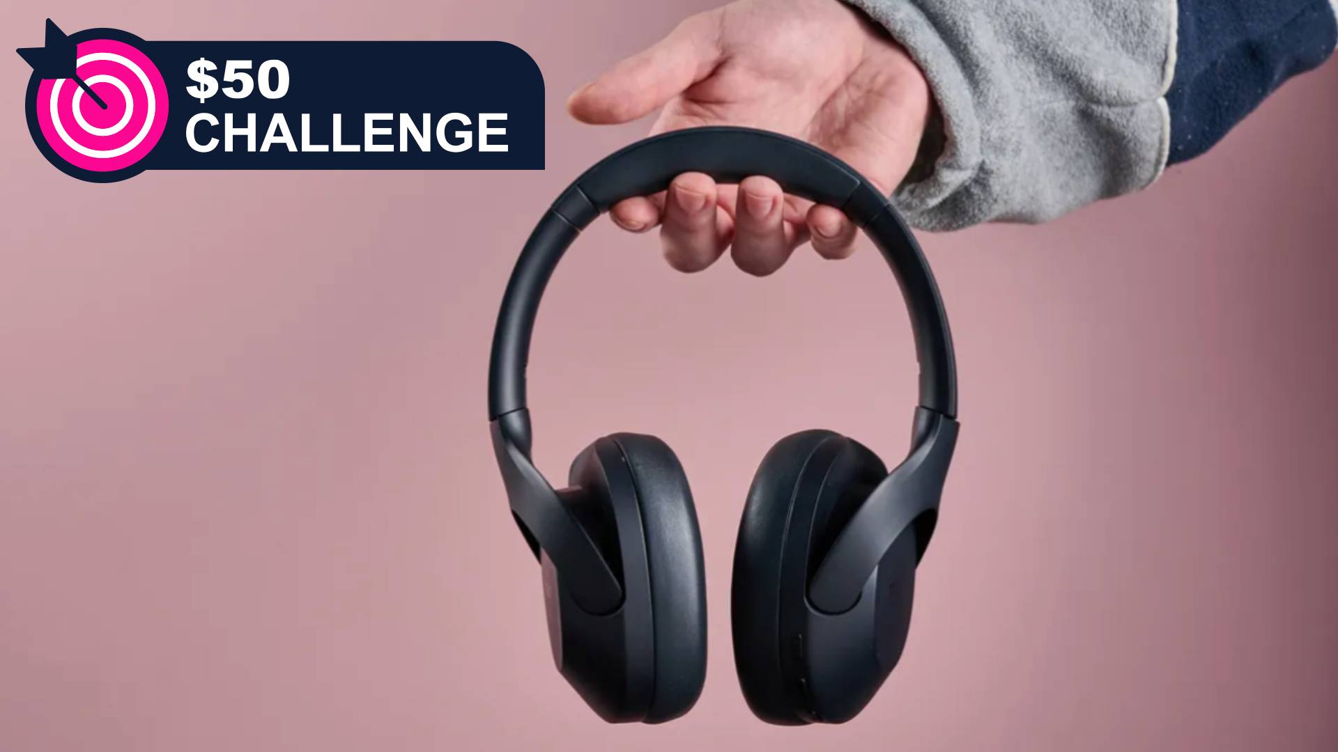 Tribit QuietPlus 81 held in a man's hand on pink background, with TechRadar's '$50 challenge' badge in the top-left corner