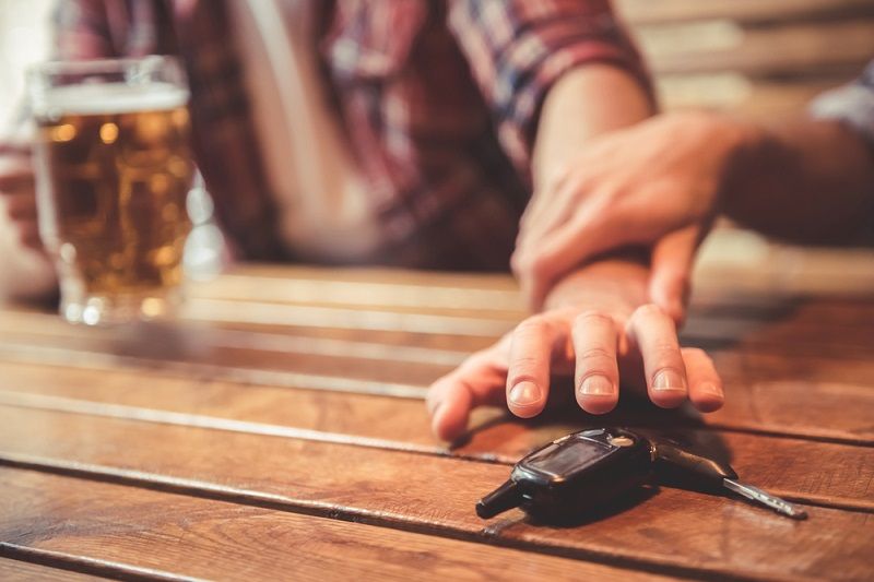 A stock photo of a man drinking while reaching for car keys while his friend stops him.