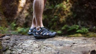 Man walking on log in forest wearing hiking sandals