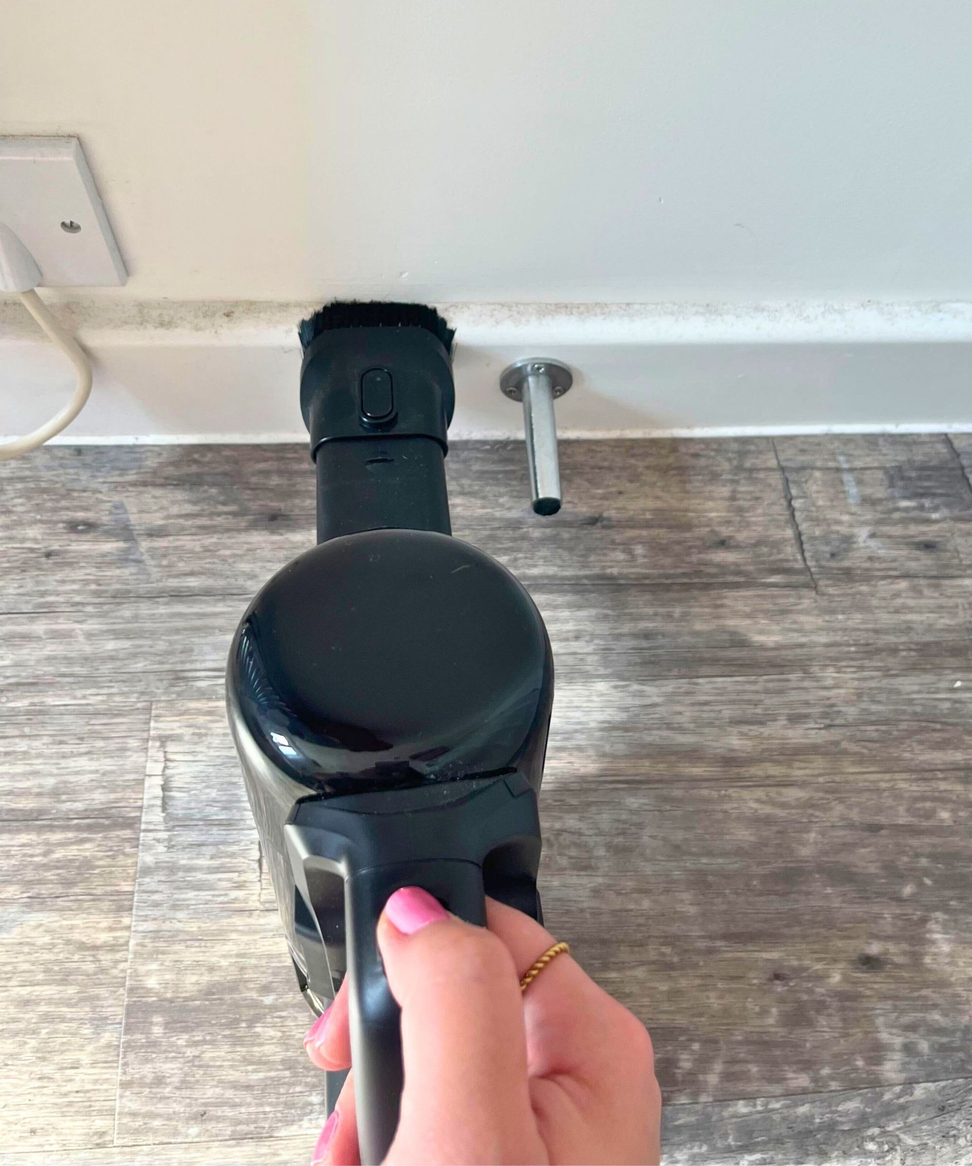 Small black handheld eufy E20 vacuum with it's bristled attachment on the dusty baseboard edge