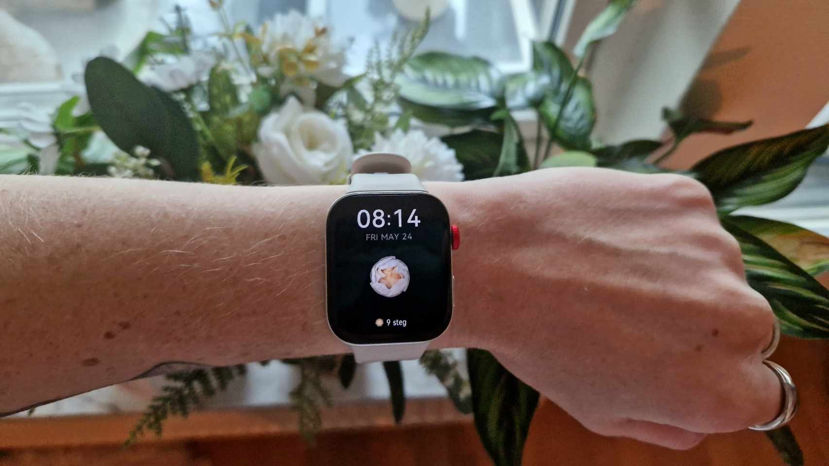 Huawei Watch Fit 3 om et håndled med nogle blomster i baggrunden.