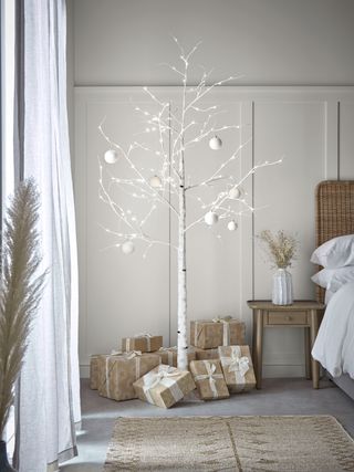 An indoor-outdoor light-up birch tree in bedroom with bed and side table