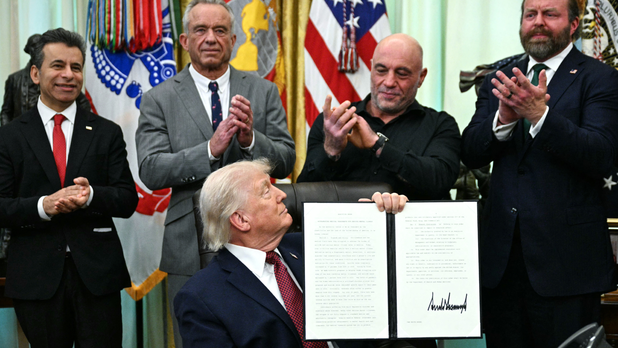 President Donald Trump looks at podcaster Joe Rogan at signing ceremony for hallucinogenics order