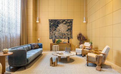 A beige living area with a grey couch, white chairs, a round coffee table, wooden console and wall paintings.