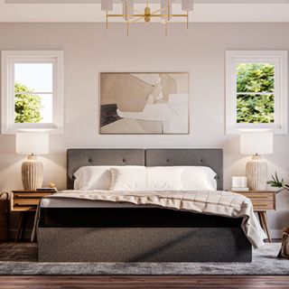 Grey bed in a neutral bedroom with gold contemporary chandelier and dark wood floors