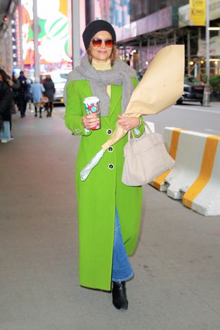 Katie Holmes walks through Times Square wearing a Wicked green coat with banana republic jeans black boots and a yellow turtleneck