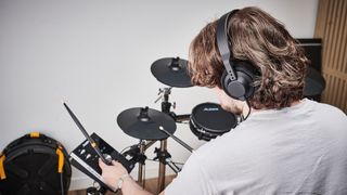 Drummer wearing headphones tweaks a parameter on an electronic drum set module