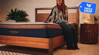 A woman sitting on Brooklyn Bedding CopperFlex mattress in sleep studio with a nightstand and plants.