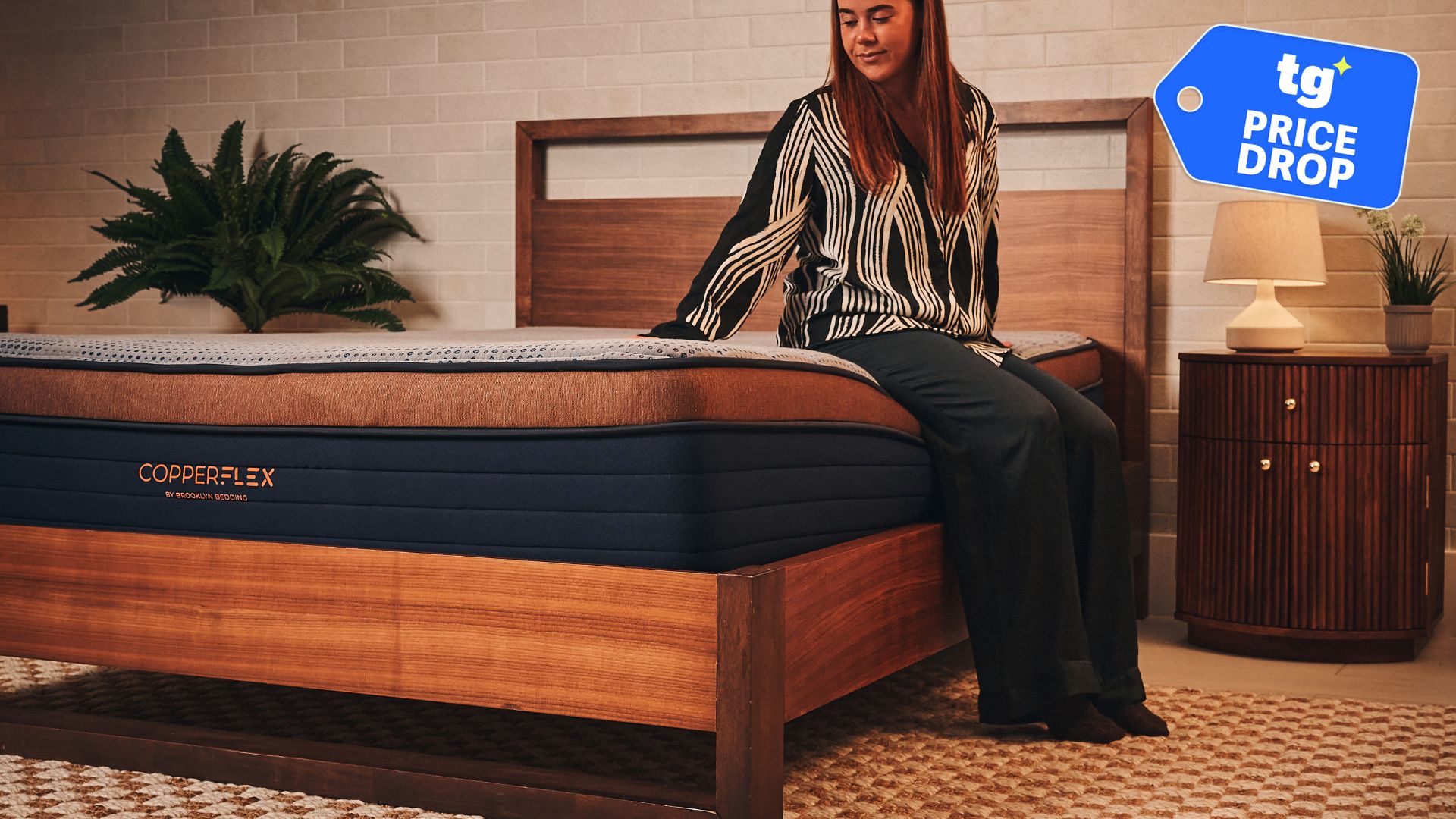 A woman sitting on Brooklyn Bedding CopperFlex mattress in sleep studio with a nightstand and plants.