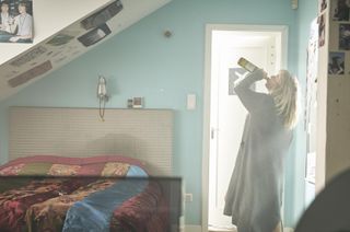 Jenna stands in her childhood bedroom (still with posters on the walls), wearing a housecoat and swigging directly from a bottle of wine