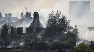A British flag flies amongst the smoldering ruins of houses as fire services tackle a large blaze on July 19 in Wennington, England. A series of grass fires broke out amid an intense heatwave.