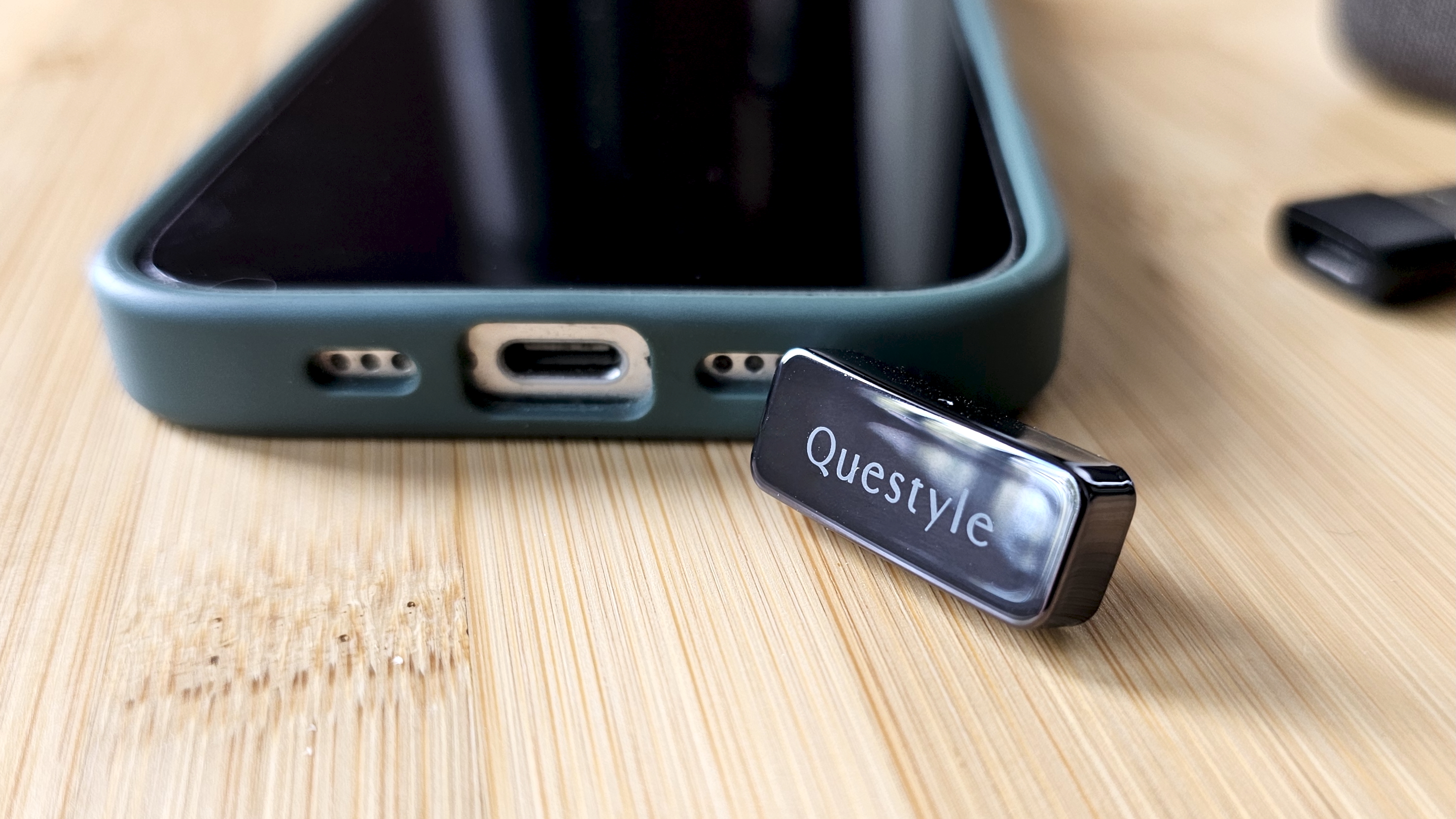 The Questyle QCC Dongle Pro with a smartphone to denote size, on a light wooden table
